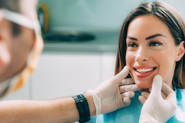 Dentist in white gloves touching smiling patient’s cheeks