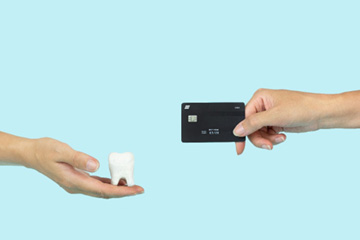 Hand holding model tooth reaching out to hand holding black credit card