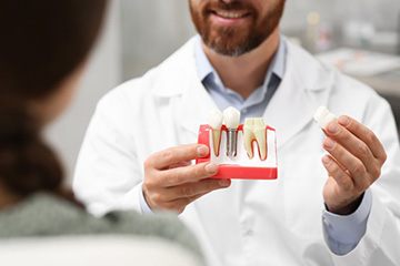a dentist holding a model of a dental implant