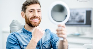 Man looking at teeth and smiling in dental chair during general dentistry visit