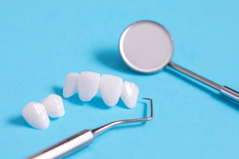 Dental mirror, cleaning tool and veneers laying on a blue background