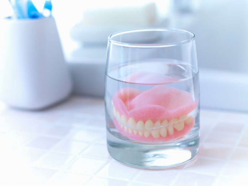 A pair of dentures soaking in a glass of water