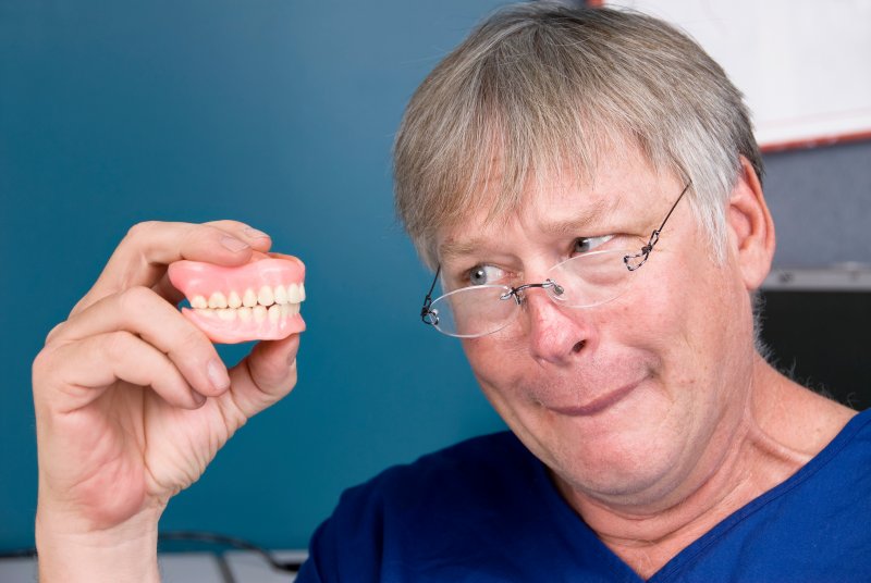 A man looking at his dentures skeptically while holding them at eye level
